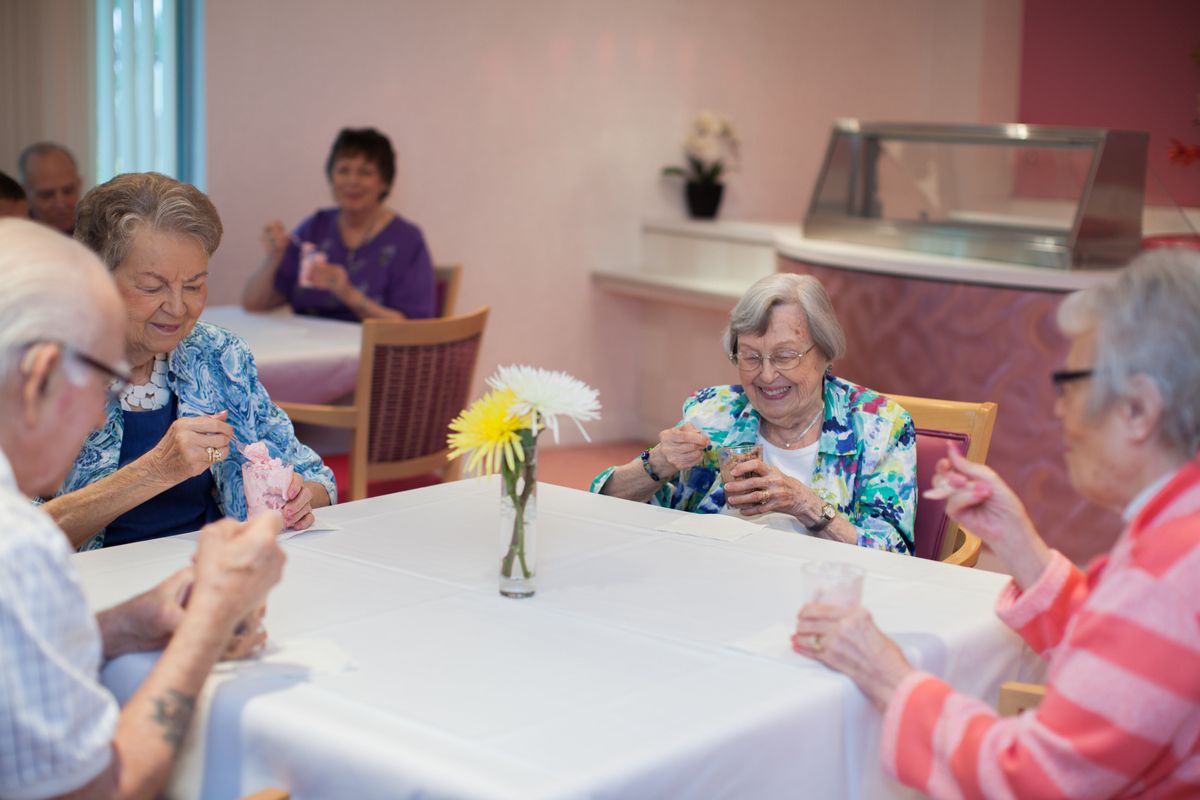 A group of elderly individuals enjoy socializing at a table in a retirement home.