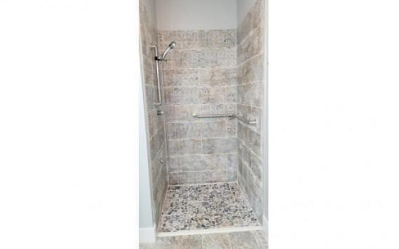 A modern shower with tiled walls and pebble flooring.