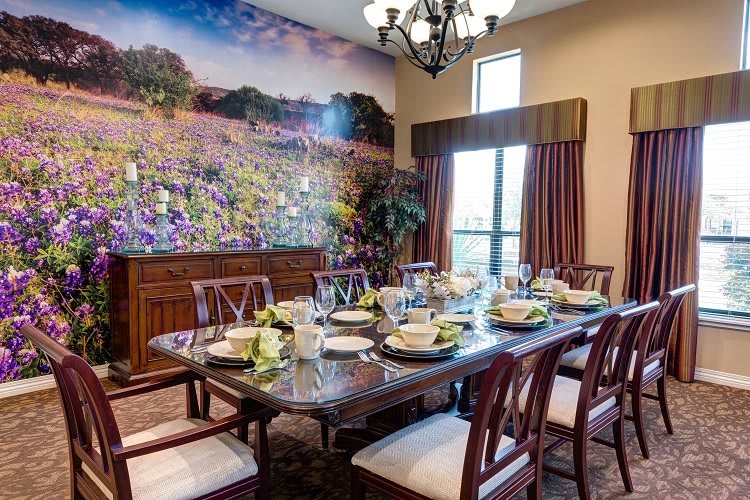 A beautifully set dining room with a long table, elegant chairs, and a scenic mural on the wall.