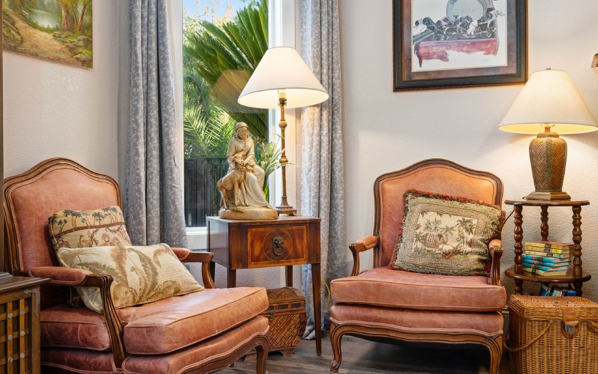 A cozy living room corner featuring vintage armchairs, a side table with a decorative lamp, and elegant cushions.