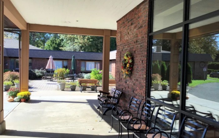 A cozy outdoor patio with chairs and a wreath on the brick wall, overlooking a courtyard.