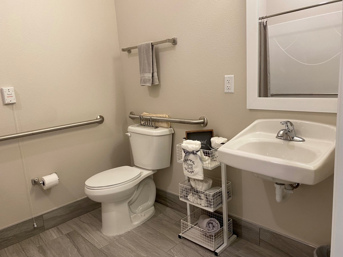 A clean and organized bathroom with a toilet, sink, and handrails.