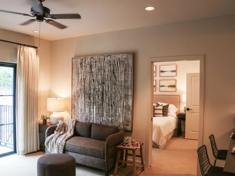 A cozy living room with a sofa, artwork on the wall, and a glimpse into a bedroom.
