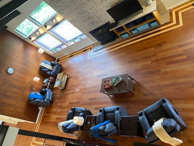 A spacious living room with hardwood floors, featuring multiple sofas, a central coffee table, and a television setup near large windows.