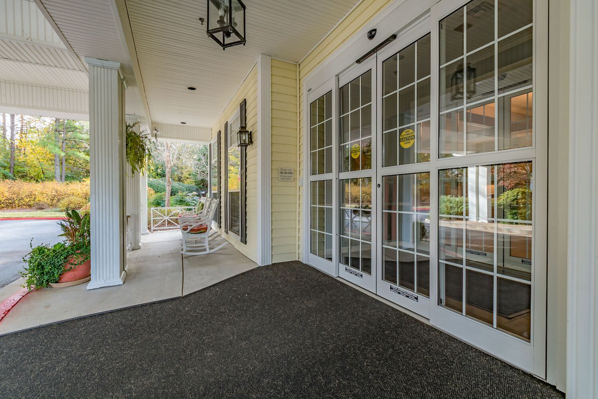 A covered entrance with sliding glass doors and a carpeted floor, leading to a porch with outdoor plants.