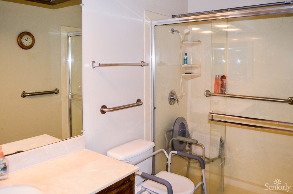 An accessible bathroom featuring a shower with handrails and a shower chair.
