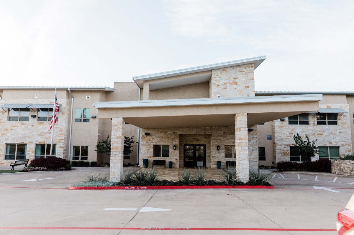 A modern building entrance with a stone facade and covered drop-off area.