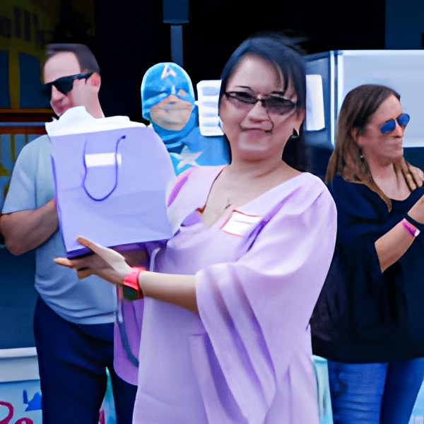 A woman holding a gift bag at an outdoor event, surrounded by other people.