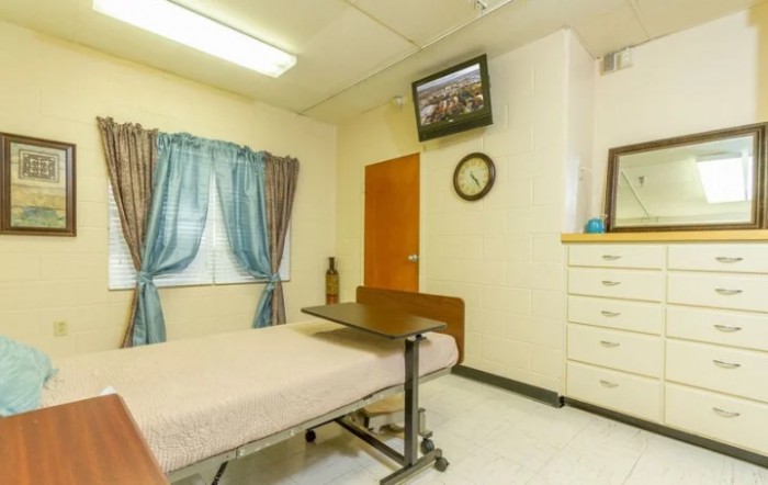 A hospital room with a bed, wall-mounted TV, window curtains, and a clock.