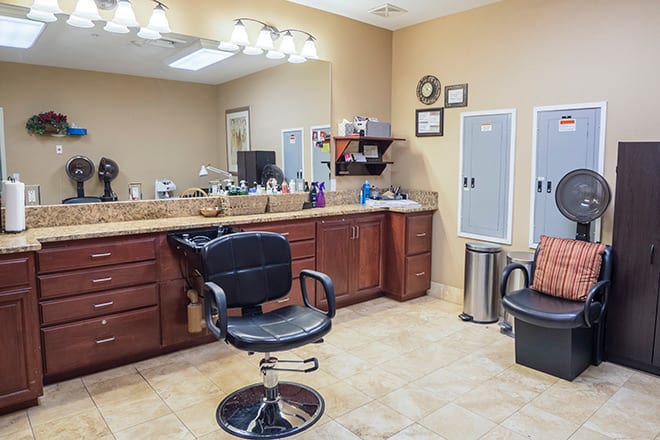 A clean and well-organized salon interior featuring a styling chair, mirrors, and cabinets.