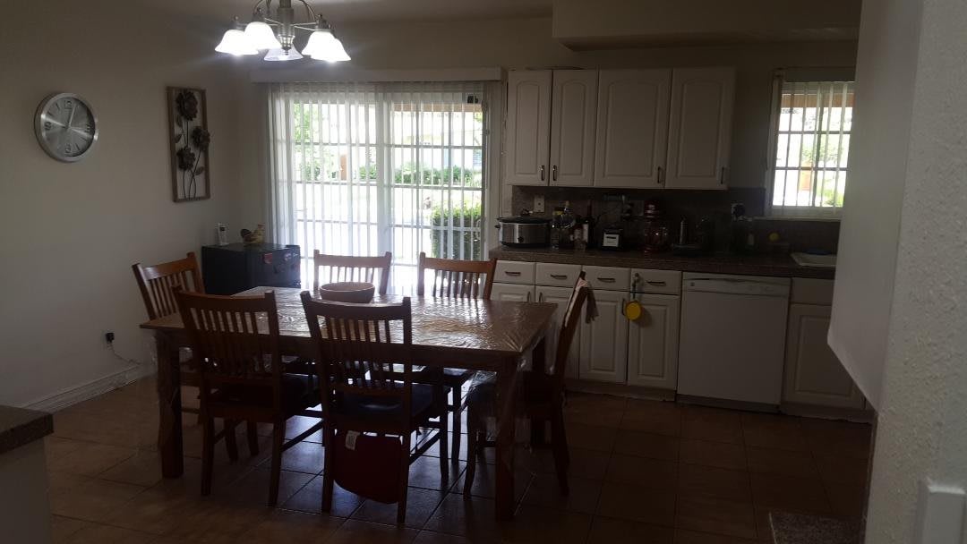 A kitchen and dining area with a wooden table, chairs, and white cabinets next to a large window.