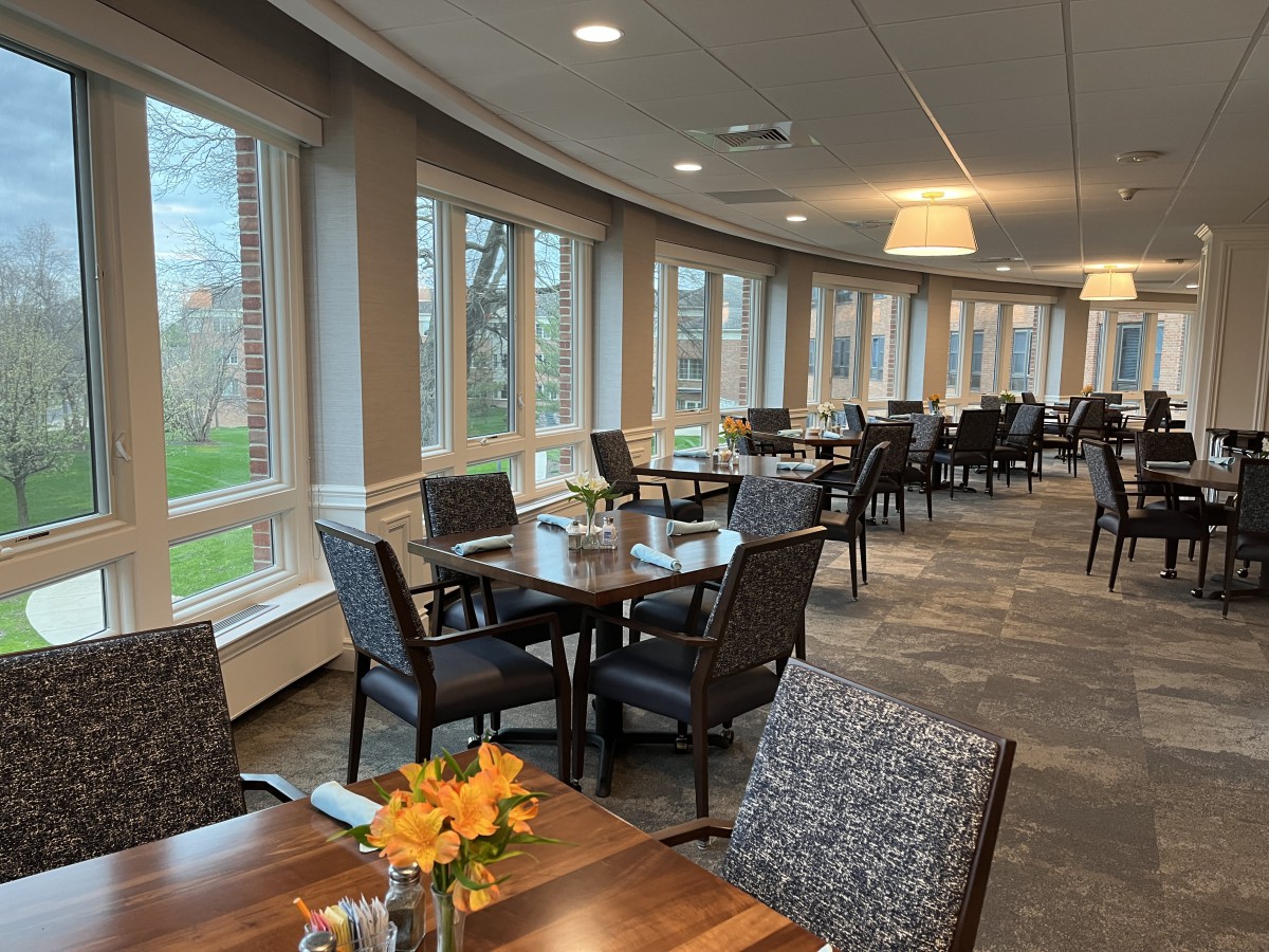 A modern dining area with neatly arranged tables and chairs, featuring large windows and decorative flowers.