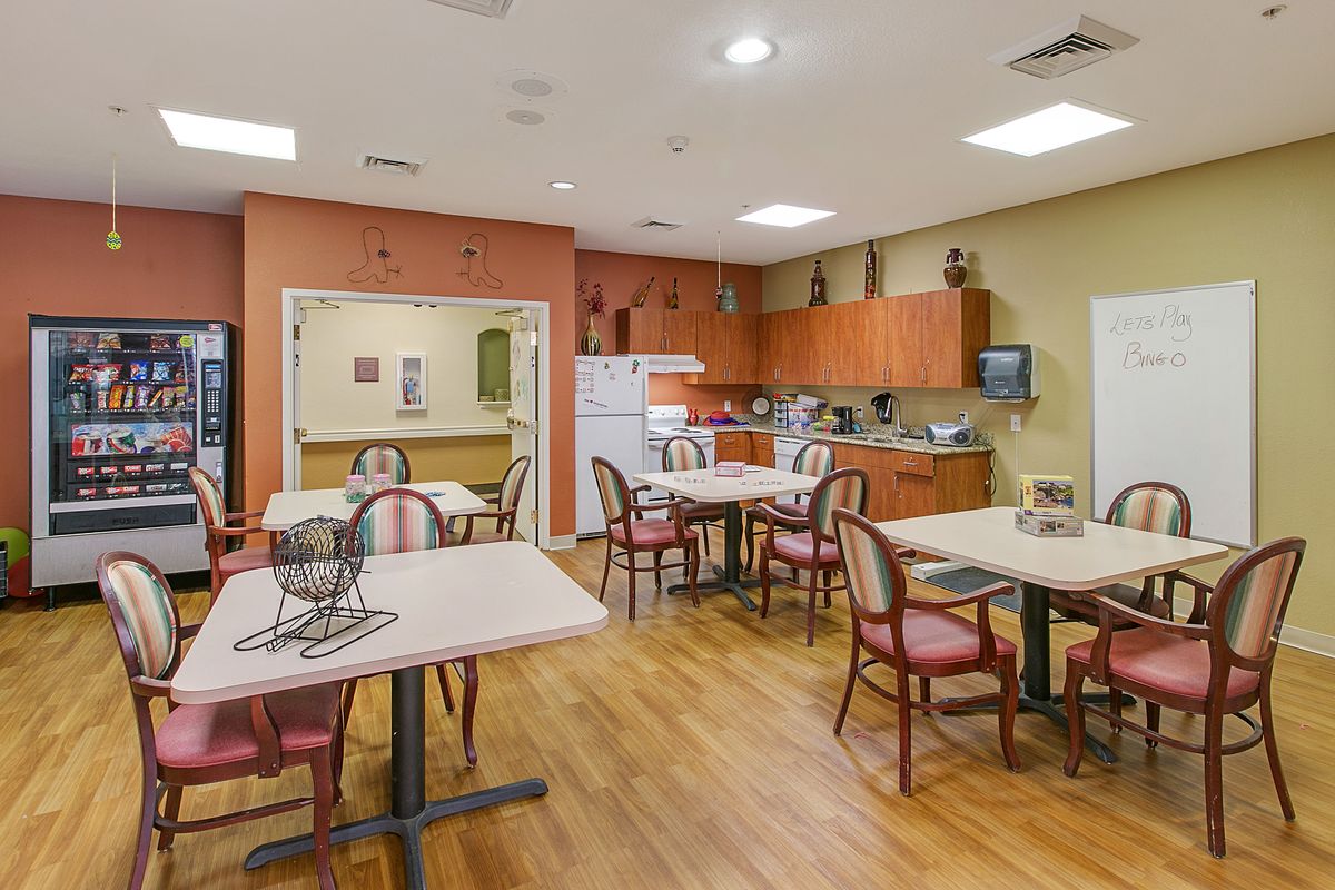 A cozy kitchen and dining area with multiple tables and chairs, featuring wooden cabinets and a refrigerator.
