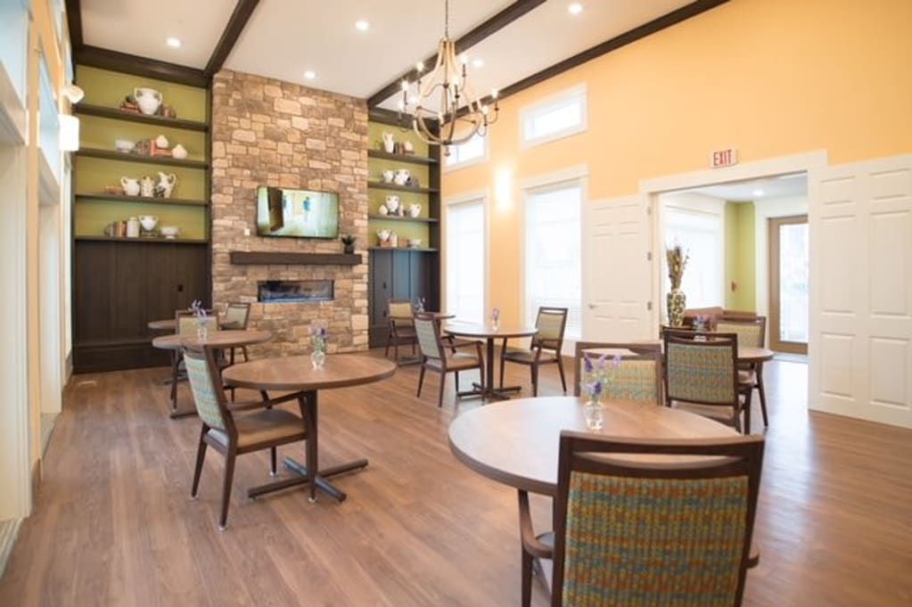 A cozy dining area featuring round tables, comfortable chairs, a stone fireplace, and elegant chandelier lighting.