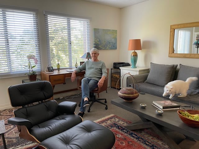 A man sits comfortably in a well-furnished living room with ample natural light.