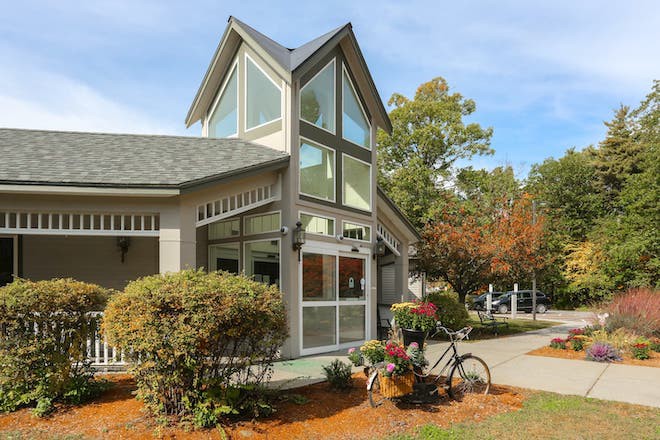 A modern building with a prominent glass facade and an outdoor bicycle stand, surrounded by greenery on a sunny day.
