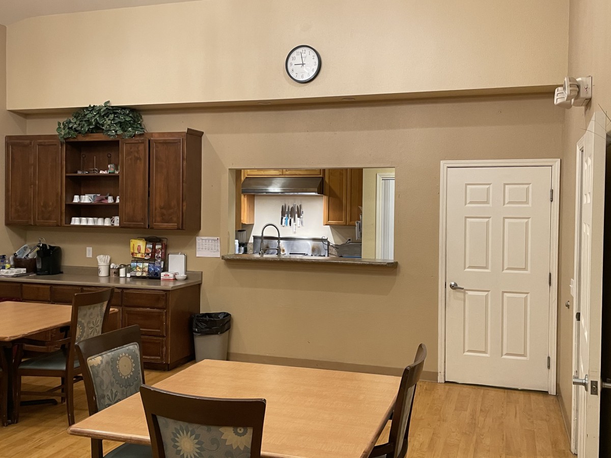 A kitchen and dining area with a wall clock, wooden cabinets, and a table with chairs.