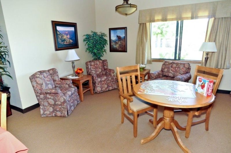 A cozy living room with floral chairs, a round wooden table, and framed artwork on the walls.