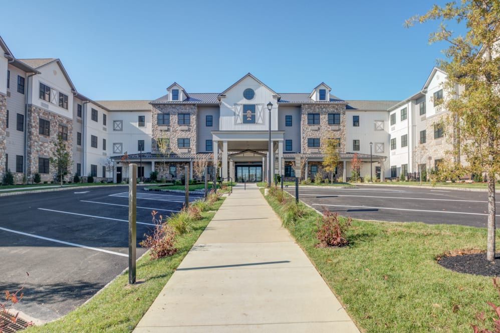 A modern hotel building with a wide entrance pathway, surrounded by a neatly maintained parking area and landscaping on a sunny day.