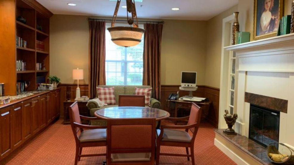 A cozy meeting room featuring a round table surrounded by chairs, a lamp, and a computer in the corner.
