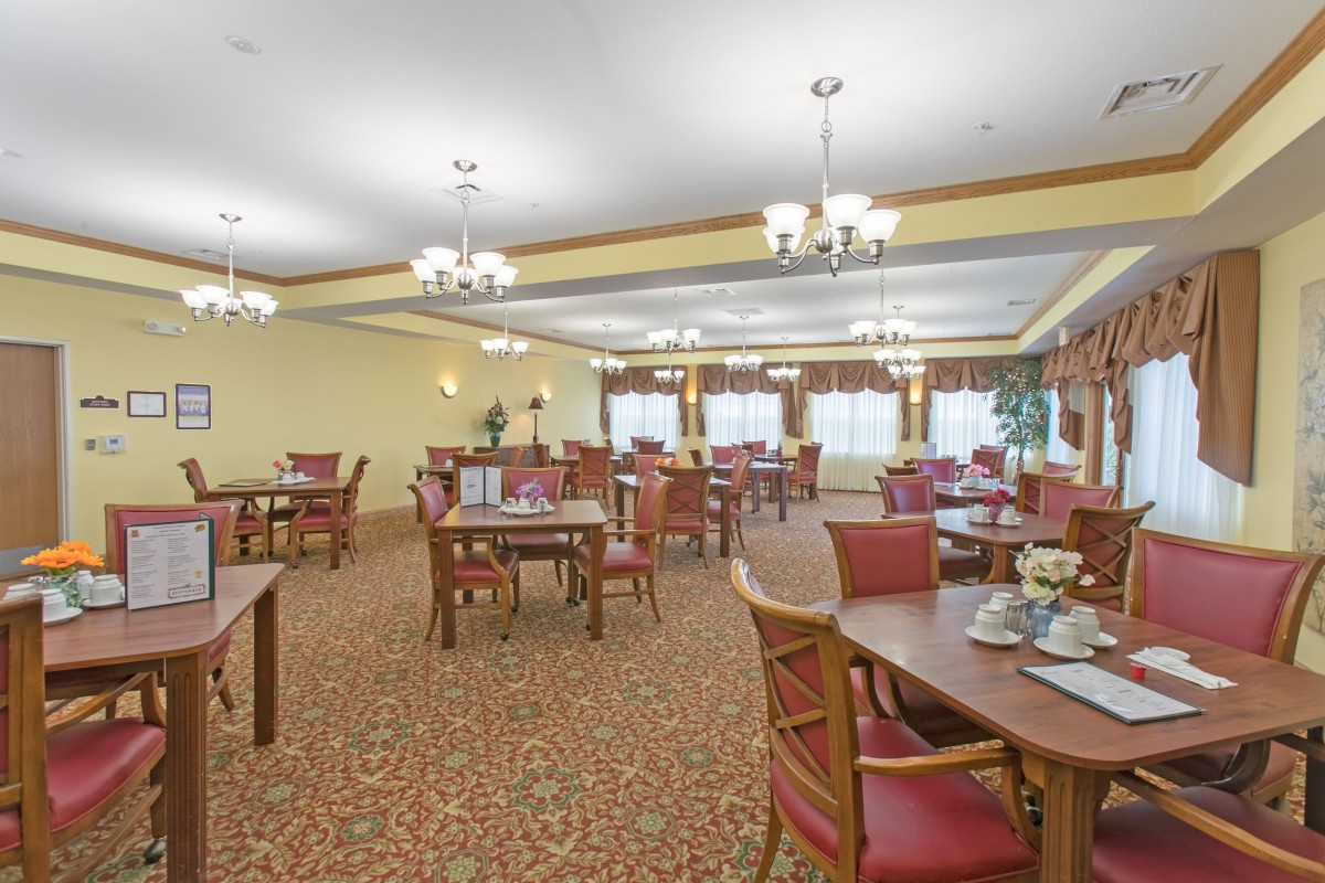 An elegant dining area with multiple tables and chairs, featuring chandeliers and a carpeted floor.