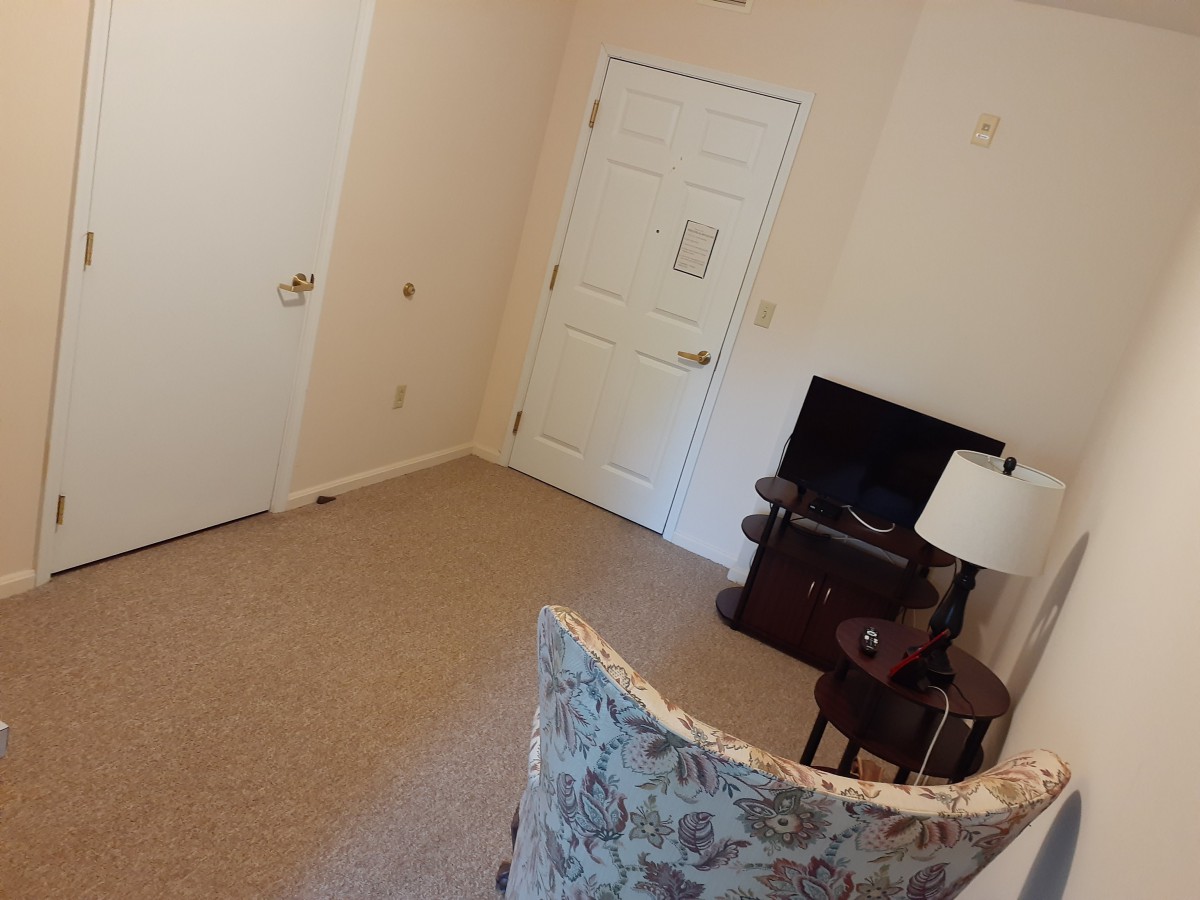 A cozy living room with a chair, television, and lamp near the door.