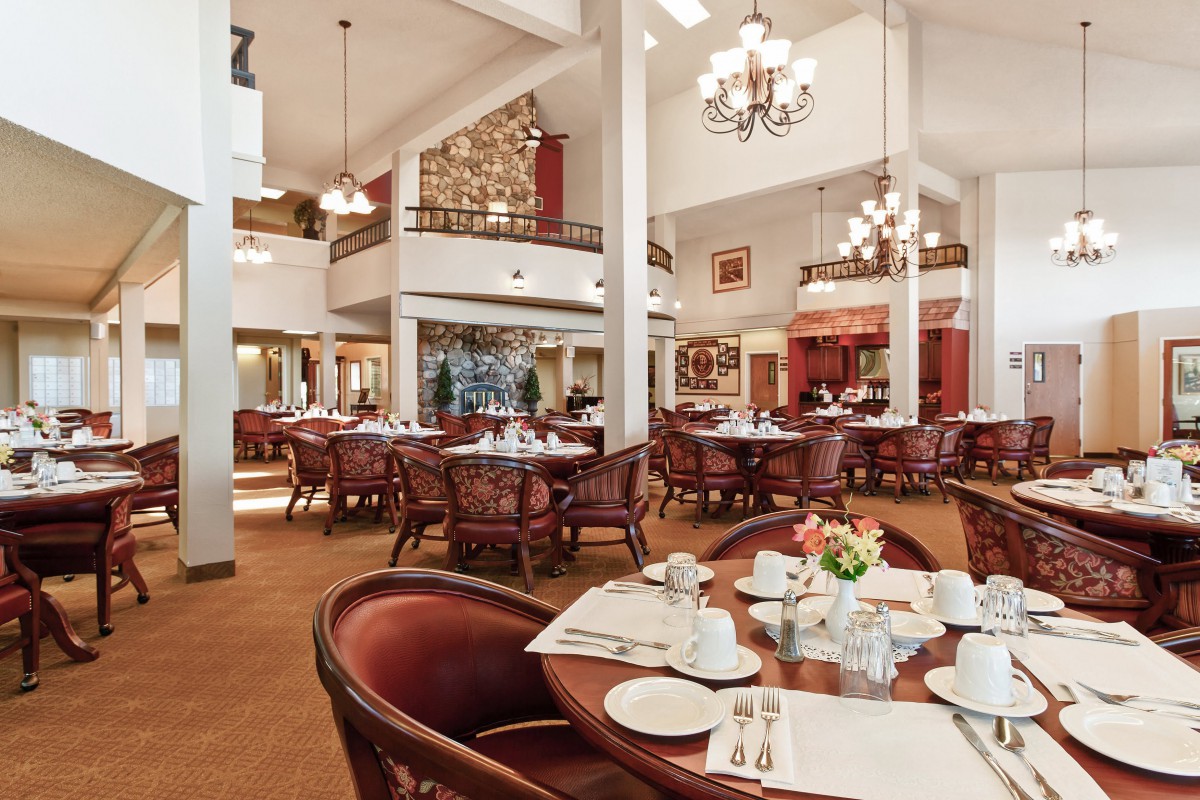 A spacious and elegantly decorated restaurant dining area with chandeliers, set tables, and comfortable seating.