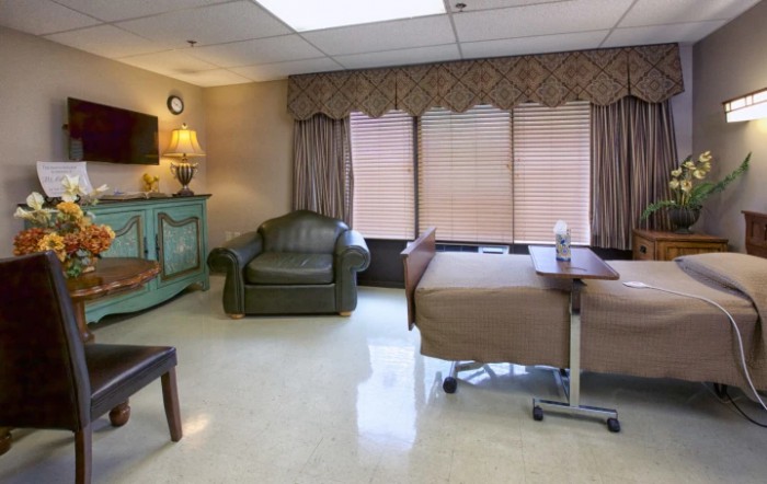 A hospital room with a patient bed, armchair, and medical equipment.