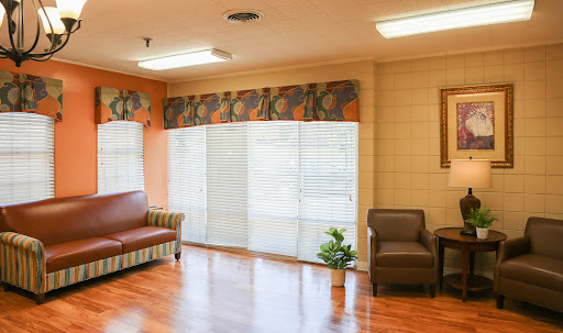 A well-lit living room with a couch, chairs, and large windows allowing natural light.