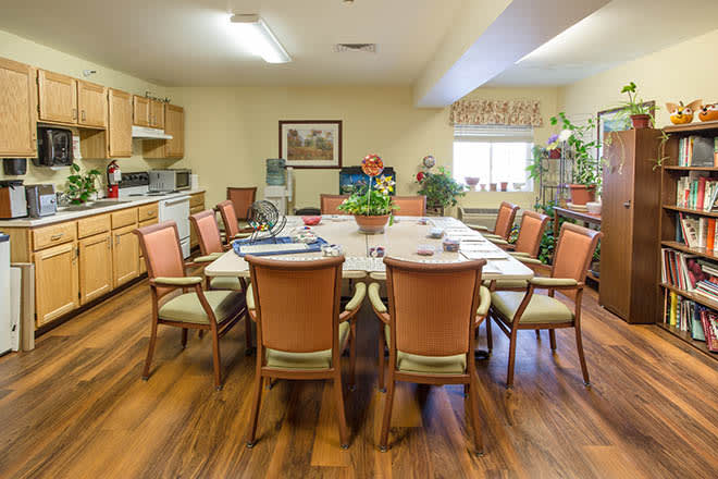 A well-furnished conference room with a large meeting table surrounded by chairs and featuring a small kitchen area.