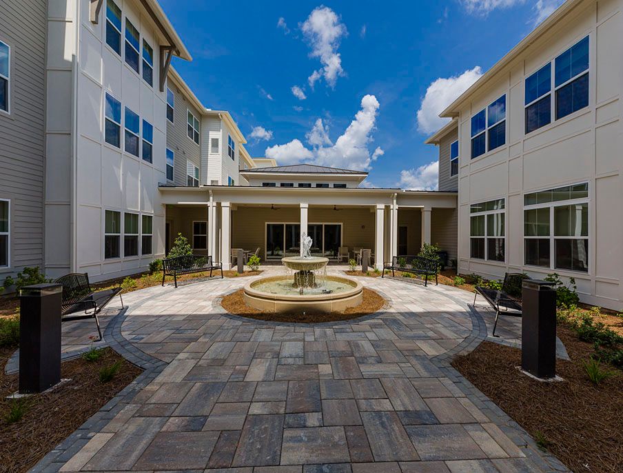 A beautiful courtyard with a central fountain surrounded by modern residential buildings under a blue sky with clouds.