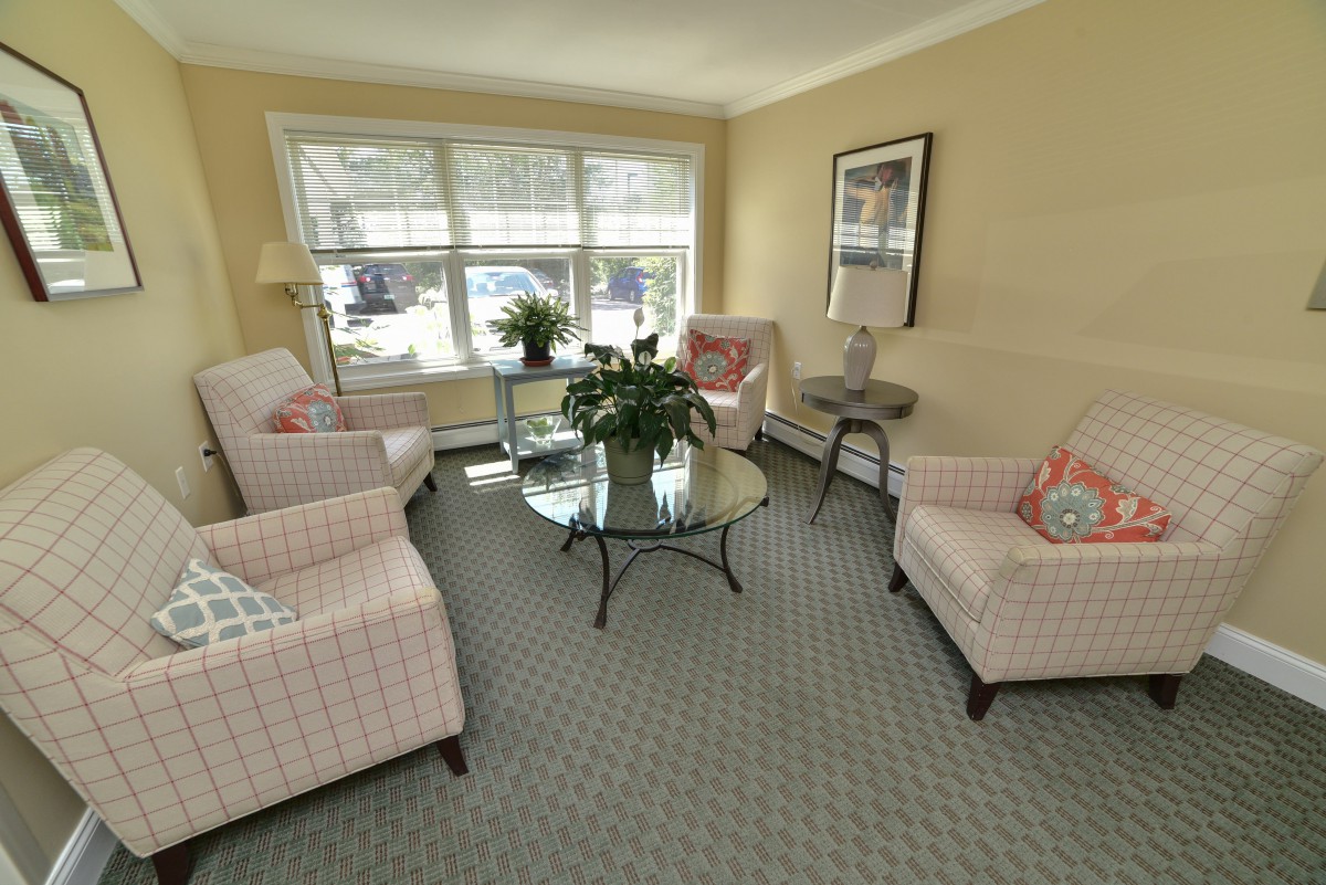 A cozy living room featuring comfortable chairs, a glass coffee table, and large windows allowing natural light.