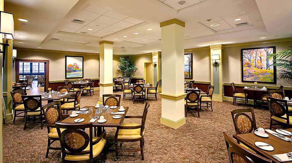 An elegant dining area with neatly arranged tables and chairs, carpeted flooring, and decorative artwork on the walls.