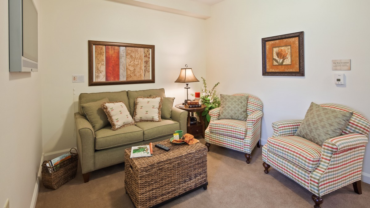 A cozy living room featuring a green sofa, two striped armchairs, a wicker coffee table, and decorative lamps and artwork on the walls.