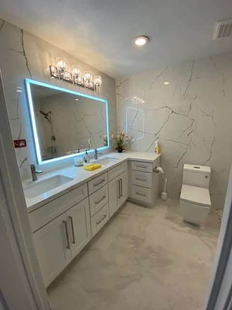 A modern bathroom featuring a large illuminated mirror, sleek vanity, and elegant tiling.