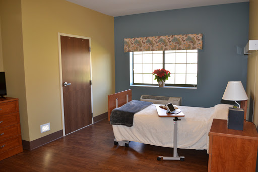 A well-lit hospital room featuring a single bed, a window with curtains, and minimal furniture.