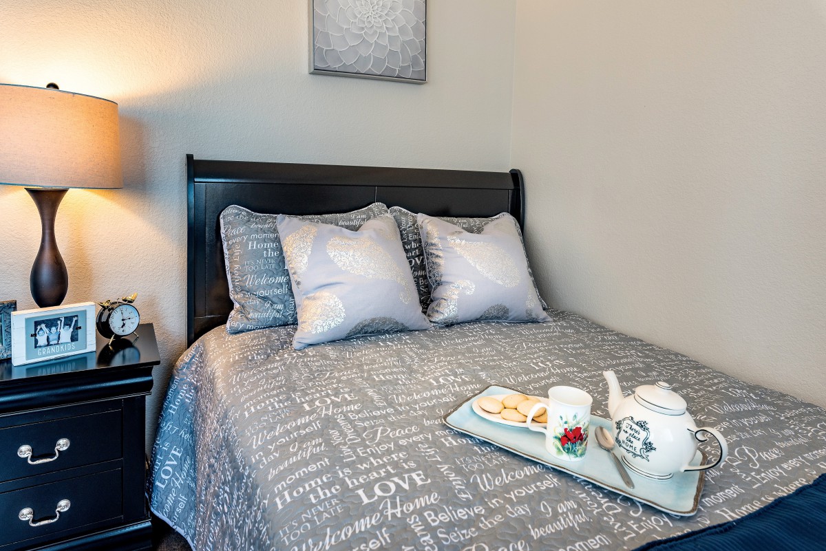 A cozy bedroom featuring a bed with patterned bedding, two pillows, and a tray with a tea set.