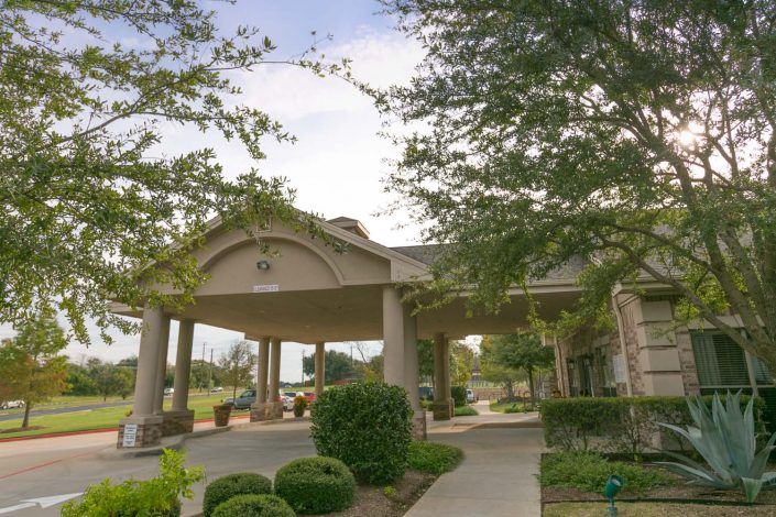 A well-landscaped building entrance featuring trees and bushes along a pathway.