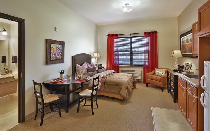 A modern bedroom interior with a bed, table, chairs, and a window with red curtains.