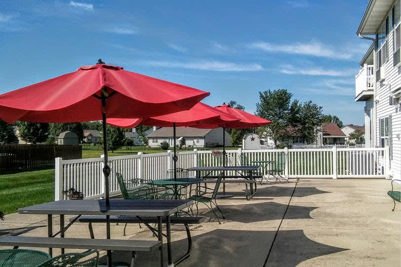 A sunny outdoor patio with red umbrellas shading tables and chairs.