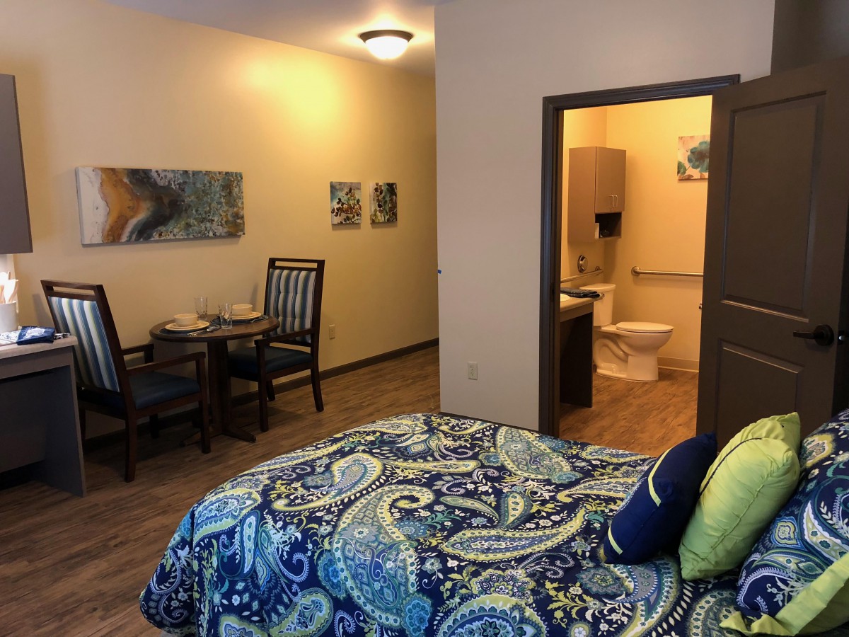 A cozy bedroom with a vibrant bedspread, an adjoining bathroom, and a small dining area.