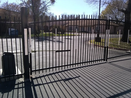 A black metal gate casting shadows on the pavement in a well-lit outdoor area.