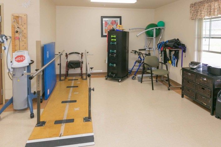 A therapy room equipped with parallel bars, a wheelchair, walkers, and other rehabilitation tools.