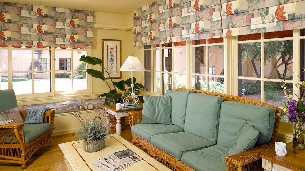 A cozy living room with a green sofa, patterned window shades, and a coffee table adorned with a house plant.