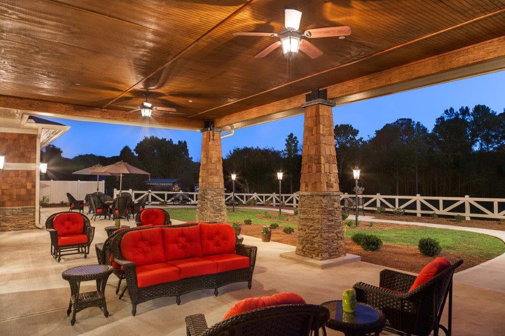 A cozy outdoor patio with red-cushioned seating, stone pillars, and warm evening lighting.