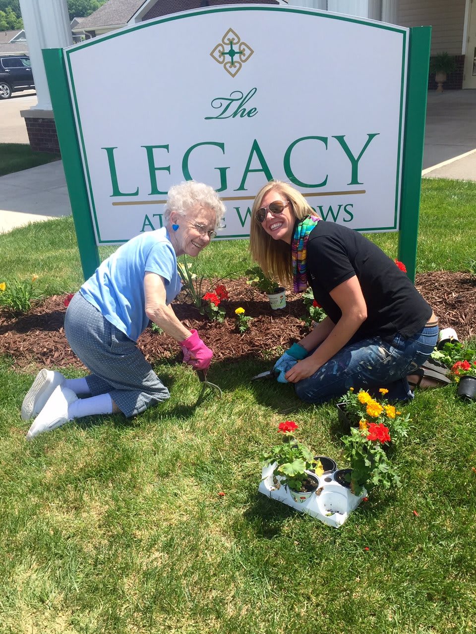 Two people gardening together in front of a sign that says 'The Legacy'.