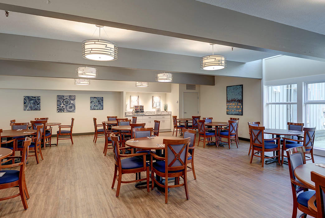 A spacious dining area with multiple tables and chairs, featuring modern lighting fixtures and a wooden floor.
