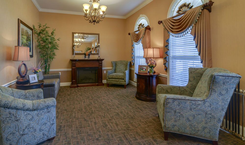 A traditional living room with elegant furnishings, featuring armchairs, a fireplace, and decorative curtains.