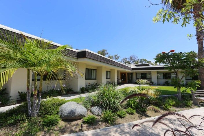 A modern single-story house with well-maintained landscaping and palm trees under a clear blue sky.