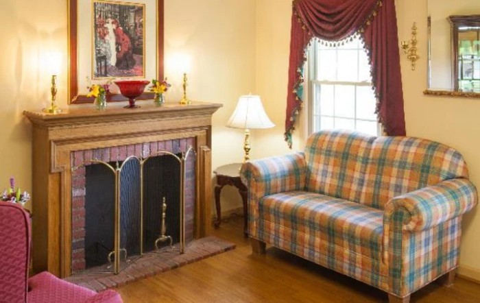 A cozy living room featuring a fireplace and plaid couch with elegant curtains.